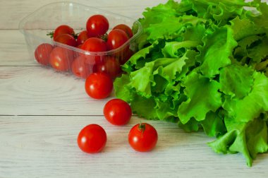Tahta arka planda bir kabın içinde taze marul ve kiraz domatesleri.