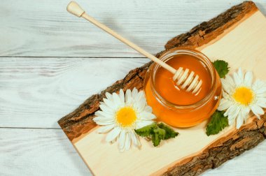 Kavanozda taze bal, tahta bir kütükte papatyalarla.