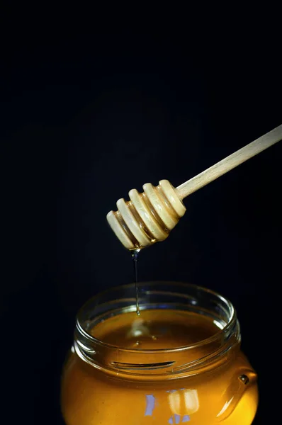 蜂蜜は黒い背景の瓶にスプーンを流し込み — ストック写真