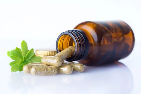 Botella de pastillas homeopáticas con algunas pastillas y hojas de hierbas Imagen de stock