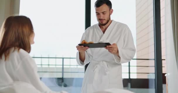 Novio lleva desayuno a mujer en cama contra ventana — Vídeos de Stock