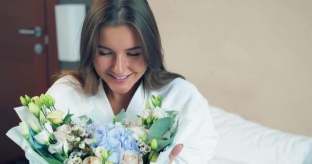 Lady em roupão olha para flores frescas sentadas em uma cama macia — Vídeo de Stock
