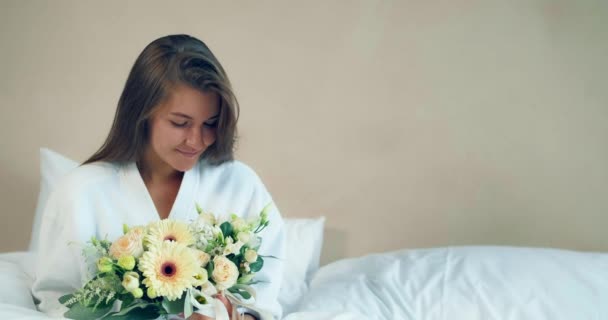 Όμορφη γυναίκα κρατά ωραία λουλούδια μπουκέτο κάθεται σε μαλακό κρεβάτι — Αρχείο Βίντεο