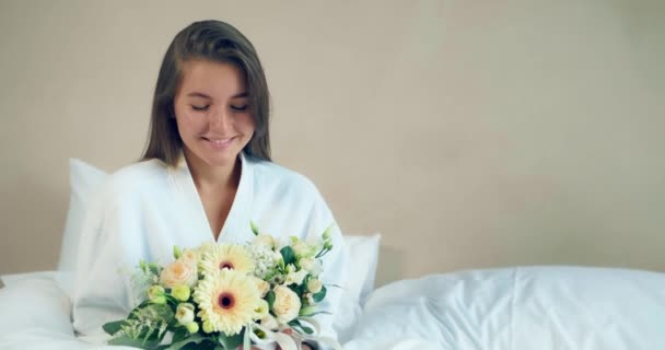 Šťastná dáma drží čerstvé květiny kytice sedí na posteli — Stock video