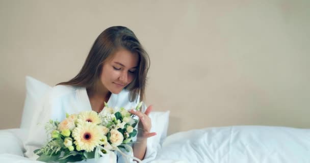 Ładna kobieta posiada ładne kwiaty bukiet siedzi na miękkim łóżku — Wideo stockowe