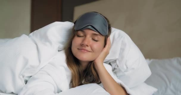 Leende kvinna i sömnmask ligger under täcke på sängen närbild — Stockvideo