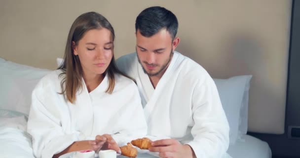 Un cuplu minunat mănâncă croissante care iau micul dejun pe pat mare — Videoclip de stoc