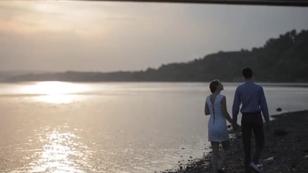 Een paar loopt een verhouding van de rivier bij zonsondergang — Stockvideo