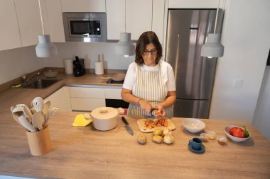Kadın mutfak tezgahında taze sebze hazırlıyor, ev yapımı yemek için havuç ve patates doğruyor. Sağlıklı beslenme, konforlu yiyecekler ve modern bir mutfakta ev hayatı..