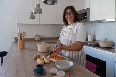 Modern mutfakta ev yapımı çorba için havuç, patates ve soğan hazırlayan kadın. Rahatlatıcı yemekler, basit malzemeler ve sağlıklı pişirme konsepti..