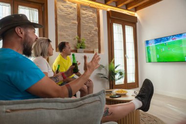 Arkadaşlar maç izlerken skor yapma anını kutluyorlar. Neşeli tepkiler, günlük yaşam tarzı, evdeki dostluk ve spor eğlencesi.