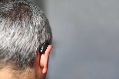 Kulağında işitme cihazı olan gri saçlı adam.