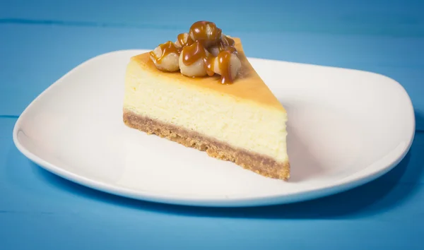 Garniture de gâteau au fromage macadamia avec du caramel sur plaque blanche sur bleu — Photo