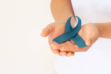 Hand holding teal color ribbon on white background with copy space. Ovarian Cancer Awareness, Gynecological, Uterine Cancer, Vulvar Cancer, Panic Disorder, Post Traumatic Stress Disorder (PTSD).