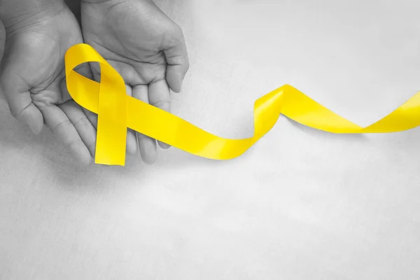 El ele tutuşan sarı kurdele beyaz arka planda, kopyalama alanı. Kemik kanseri, Sarkoma Bilinci, çocukluk kanseri, kolanjiyokarsinom, safra kesesi kanseri, Dünya İntihar Önleme Günü. Sağlık kavramı.