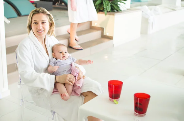 Mom in a spa with newbown baby wear white bathrobe drink tisane — Stock Photo, Image