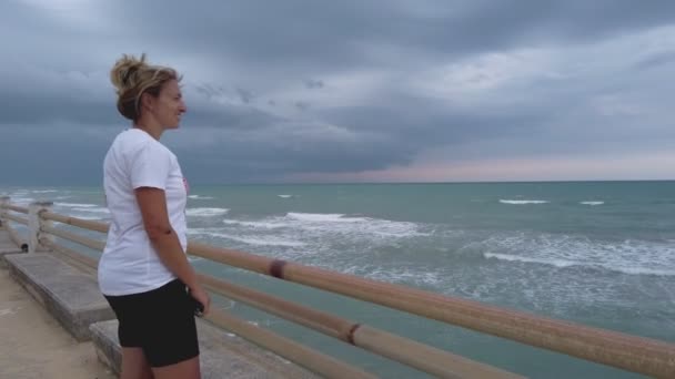 Konzept des positiven Denkens - alleinstehende Frau starrt auf stürmische und windige See und lächelt allein — Stockvideo