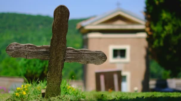 Vieja cruz de madera en el cementerio con pequeña iglesia en el día soleado con niña corriendo en el fondo — Vídeo de stock