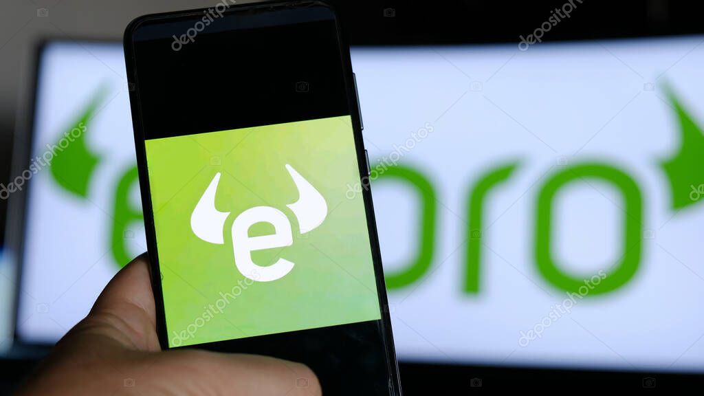 Using Etoro app. E-Toro is an to monitor equities rates for trader broker workers in stock exchange market from smartphone with monitor background in Bologna, Italy, 10 Oct 2020