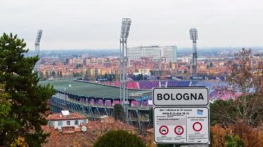 sign next to San Luca Porticoes entrance to Italian city of Bologna, in background the typical red roofs , stadium and Maggiore Hospital