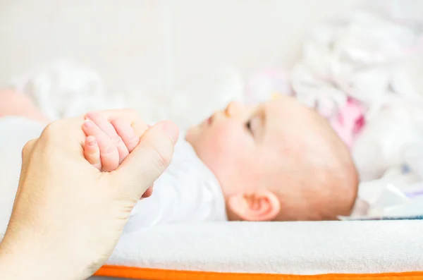 Возьмите за руку ребенка, лежащего на пеленальном столе — стоковое фото