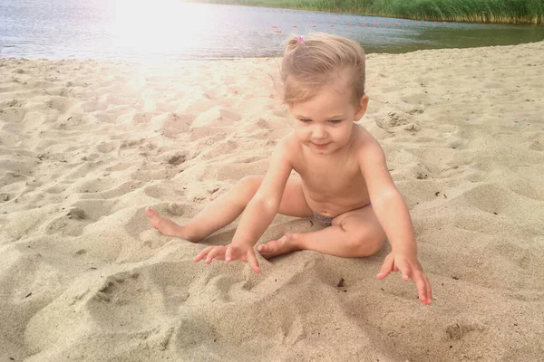 夏天的一天，一个一岁的小女孩在海滩上打沙子 免版税图库照片