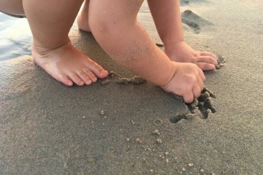 Bir yaşındaki bir çocuk kumsalda ıslak kum oynuyor.