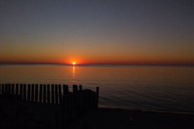 Denizde muhteşem bir gün batımı. Güneş suya, koyu mavi gökyüzüne ve denize yansıyor. Kıyıdaki ahşap eski binalar