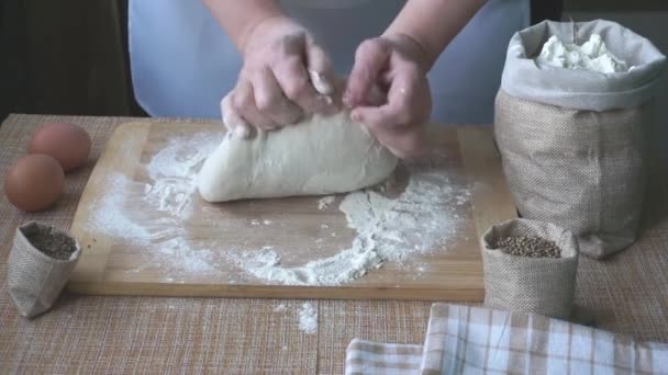 Tangan seorang wanita tua berlutut adonan untuk roti di papan kayu di atas meja, di atas meja ada 2 telur, ada kantong linen dengan rempah-rempah jintan dan ketumbar dan tepung. Hari Roti Sedunia — Stok Video