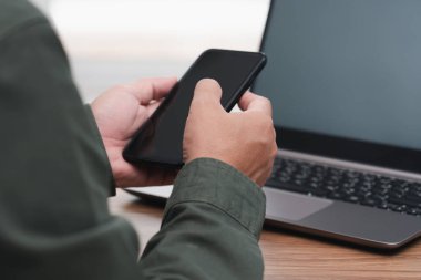 İşadamı elinde akıllı telefon tutuyor, internette çalışıyor ve ofiste çalışan masaüstü bilgisayarını kullanıyor.