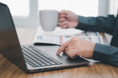 Bir adam bilgisayarın fare altlığına dokunur ve ofiste çalışırken kahve fincanını tutar.