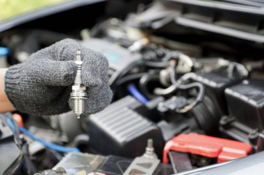 Car spark plug in a hand of Technician and engine room blur background service concept clipart