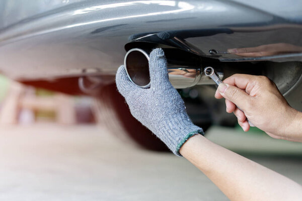Hand a man catch car exhaust and use open-end wrench for service in concept maintenance car in garage