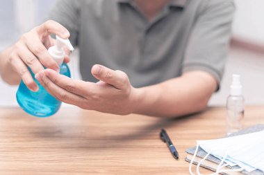 Bir adam el temizleme elini ve maskesini ahşap masada her gün antivirüs koruması için kullanır.