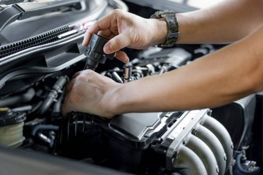 Elinizdeki buji bobinini kapatın. Garaj ve makine dairesi arka planındaki benzinli motor servisinden bir adam çıkarıldı.