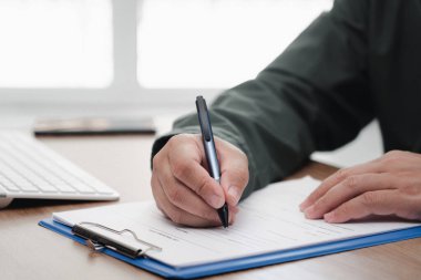 Bir adam, ofis masasındaki beyaz ataç dosyasına kalem yazısı ve klavye akıllı telefonu kullanıyor.