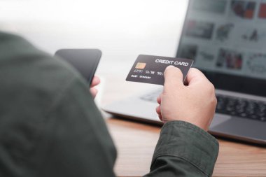İşadamı internet bankacılığı yapıyor, ödeme yapıyor ya da internetten satın alıyor kredi kartı bilgilerini akıllı telefondan giriyor ve bilgisayarını masada çalışırken kullanıyor.