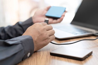 İş adamı, önemli bilgisayar bilgilerini iş yerinde tutmak için USB kablosu ile dizüstü bilgisayara bağlı harici disk kullanır 