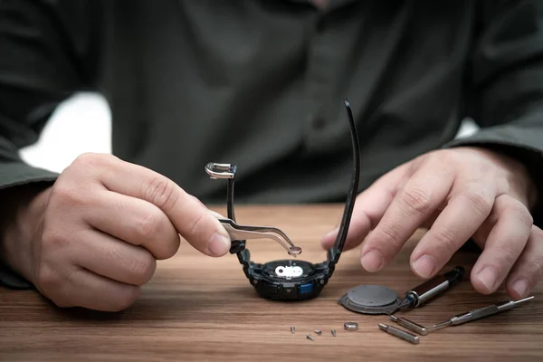 木製のテーブル上の壊れた腕時計やツールを修復する際にデジタル時計のバッテリーを削除し 変更をクランプするためにペンチを使用します — ストック写真