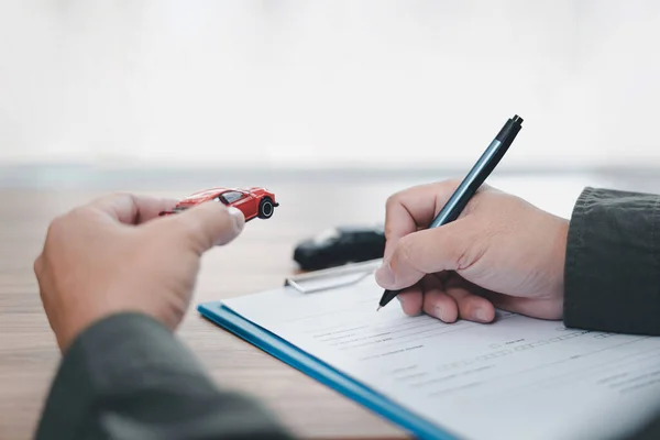 自動車保険の概念 男はペンを使用木製のテーブルと手のおもちゃの車のモデルに保険書類を書き込みます — ストック写真