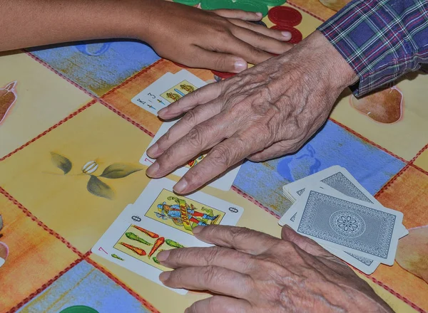 Hands of grandfather and grandson playing cards with a Spanish deck and with colored chips from the game of poker