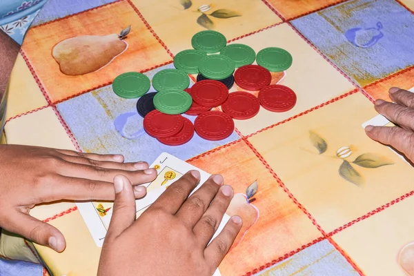 Child\'s hands playing cards with a Spanish deck and with colored chips from the game of poker