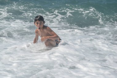 Çocuk muhteşem bir dalganın yanında suda oynuyor.