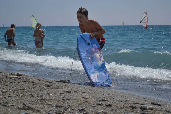 Chłopiec Wychodzący Morza Deską Surfingową Otoczony Innymi Pływakami Deskami Surfingowymi — Zdjęcie stockowe