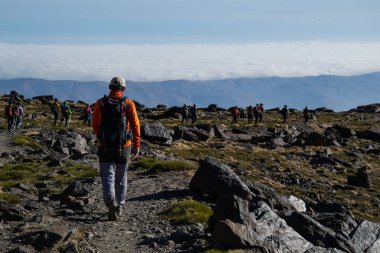 Ön planda bir yürüyüşçü kayalarla çevrili ve arka planda daha fazla insan Sierra Nevada 'da alçak bulutlar denizinde.