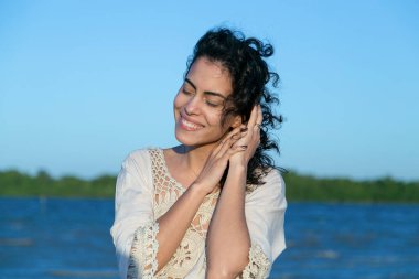 Gün batımındaki güzel esmer kadının gülümsemesi. Saçları rüzgarda savruluyor. Kıvırcık saçlı. Yaşam tarzı. Altın saat. Parnaiba Nehri Deltası.