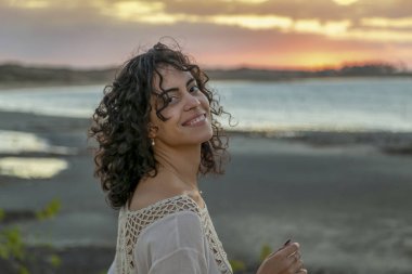 Gün batımında kumsalda yürüyen model bir esmer kadın. Saçları rüzgarda savruluyor. Kıvırcık saçlı. Yaşam tarzı. Altın saat. Parnaiba Nehri Deltası. Brezilya.