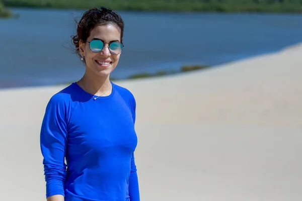 Tourism in the  Delta of Parnaiba River in northeastern Brazil. Dunes and paradisiacal landscapes. The brunette woman on the beach using sunglass. Curly hair in the wind.