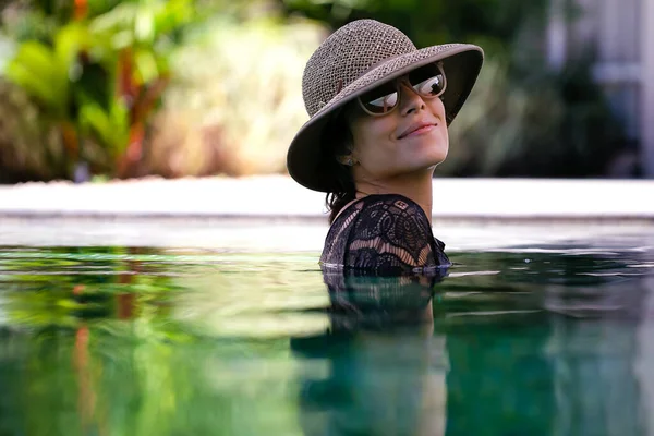 一位身穿黑色花边比基尼 头戴草帽 戴着太阳镜的女士在游泳池里摆姿势 巴西女孩休闲 健康的生活 — 图库照片