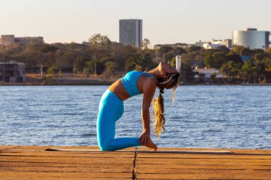Alacakaranlıkta gölün kenarında yoga yapan sarışın bir kadın. Vücut sağlığı. Yaşam tarzı. Arka planda Brezilya 'nın Brasilia kenti.